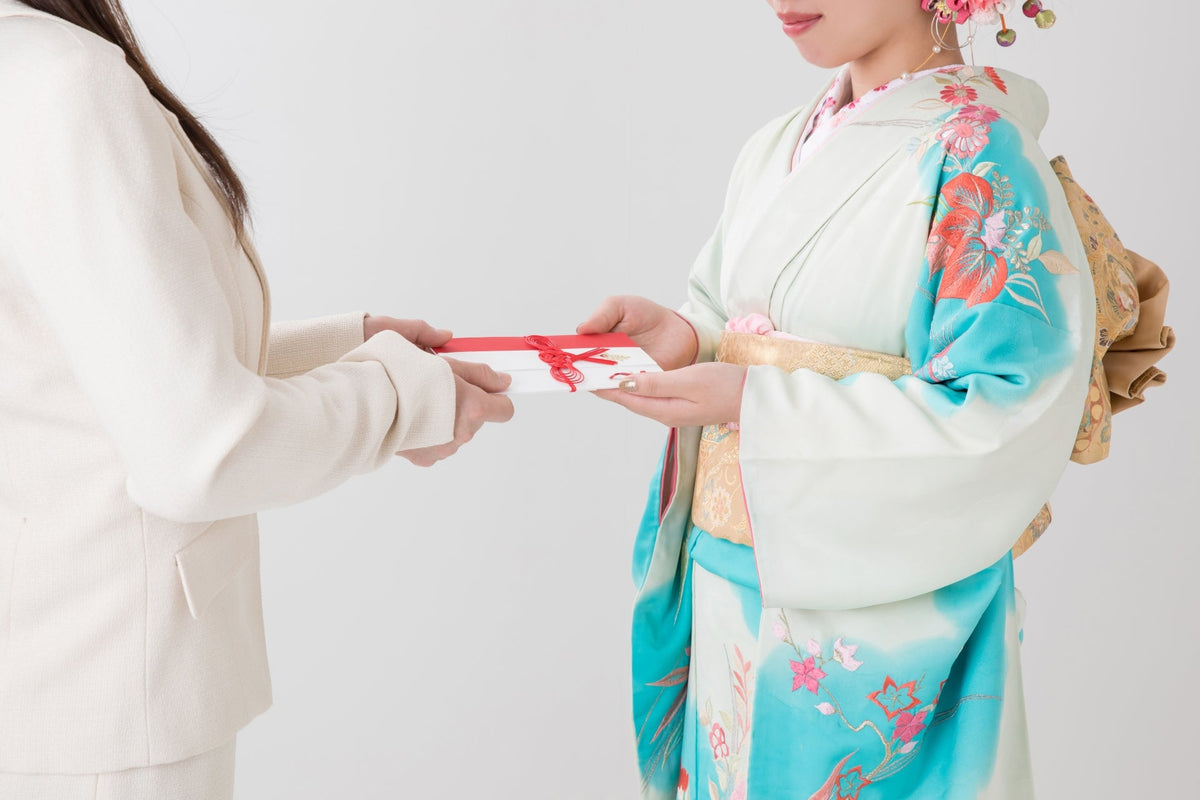 振袖を着た女性が、赤いリボンを掛けた白い封筒を両手で受け取っている