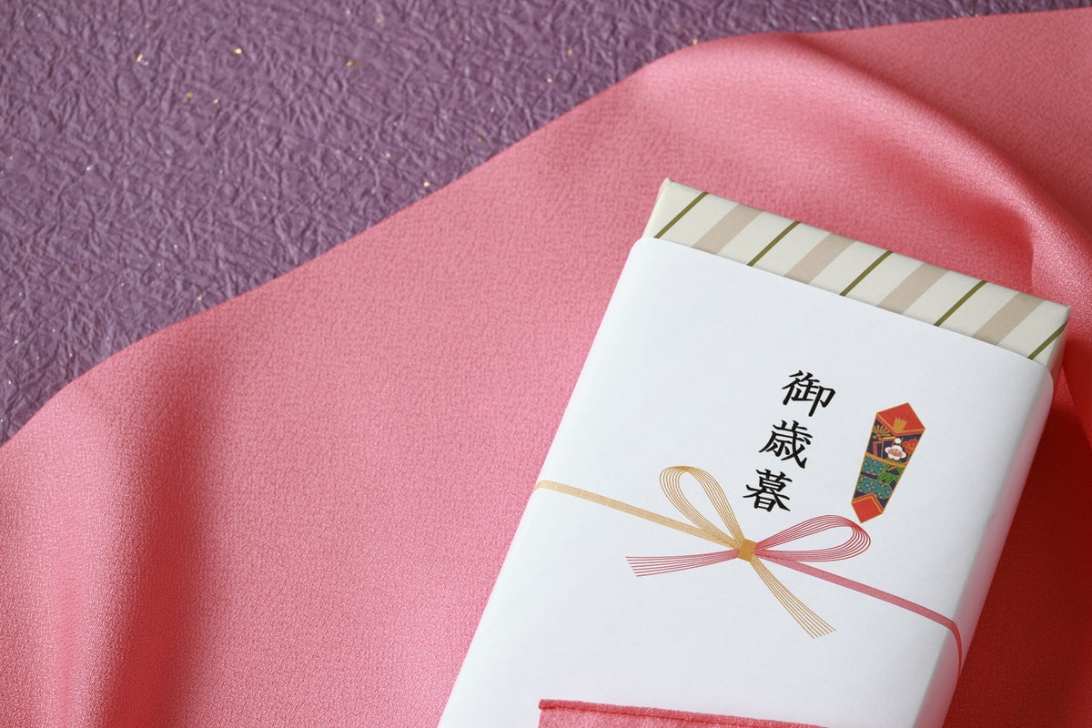 ピンクの布の上に置かれた、「御歳暮」ののし紙と紅白の水引を掛けた箱
