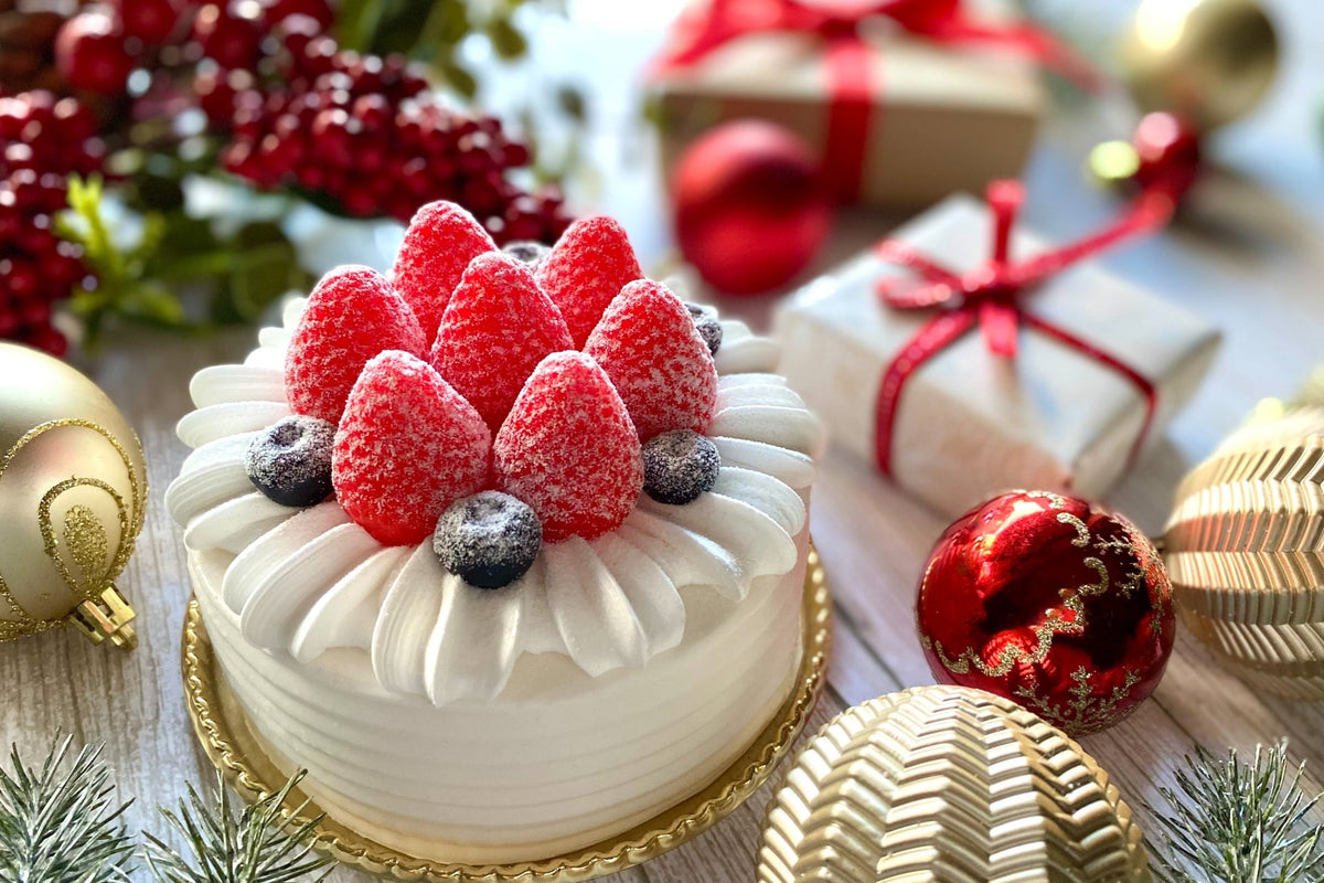 いちごとブルーベリーをのせた白いクリスマスケーキと、赤いオーナメントやリボンを掛けた贈り物の箱