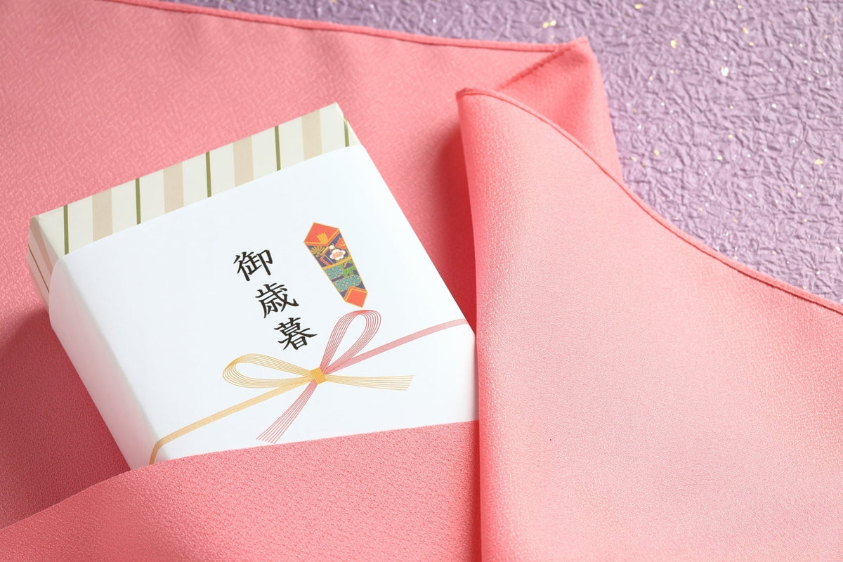 「御歳暮」と書かれたのし紙を掛けた箱を、ピンクの袱紗で包みかけているところ