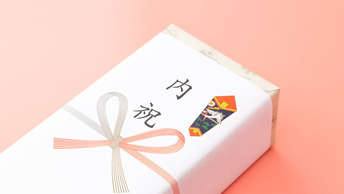 サーモンピンクの背景に置いた、「内祝」と書いたのし紙と紅白の蝶結びの水引を掛けた白い箱