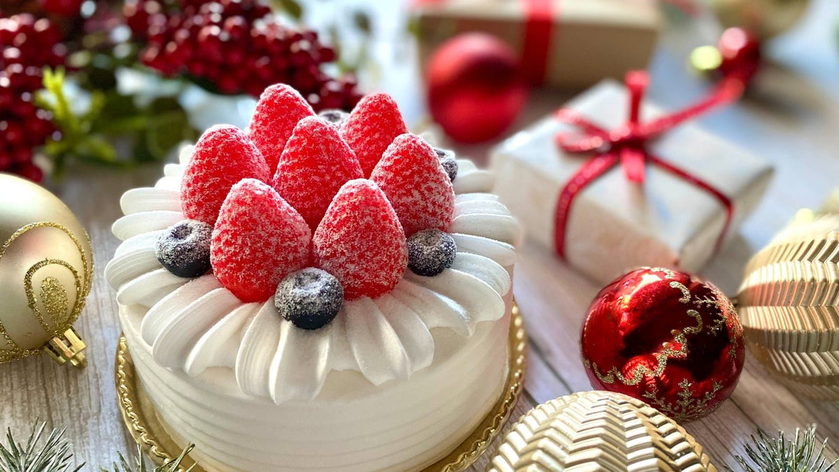 いちごとブルーベリーをのせた白いクリスマスケーキと、赤いオーナメントやリボンを掛けた贈り物の箱