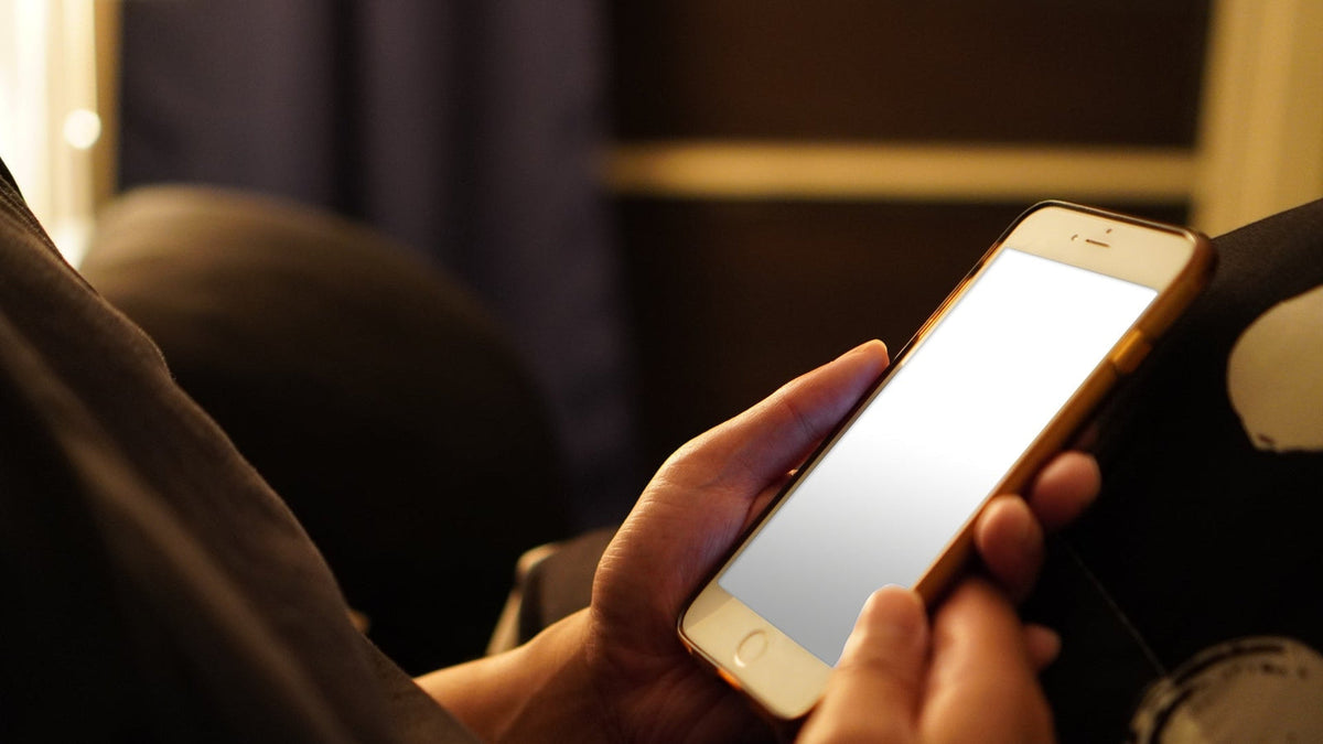 薄暗い部屋で、スマートフォンを両手で持つ手元