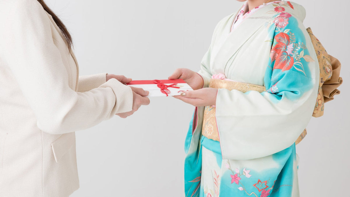 振袖を着た女性が、赤いリボンを掛けた白い封筒を両手で受け取っている
