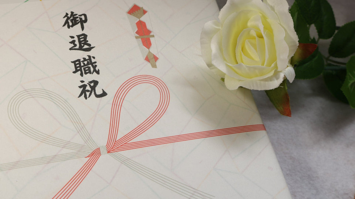 「御退職祝」と書かれた紅白の蝶結びの水引ののし紙と、白いバラ